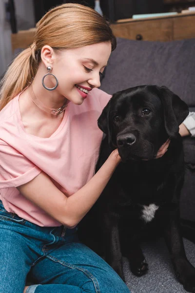 Young smiling woman embracing black labrador on sofa at home — Stock Photo