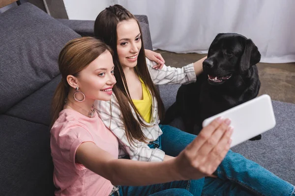 Smiling woman taking selfie with female friend and black labrador at home — Stock Photo
