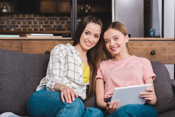 Sorridenti giovani amiche con tablet digitale sedute sul divano di casa — Foto stock