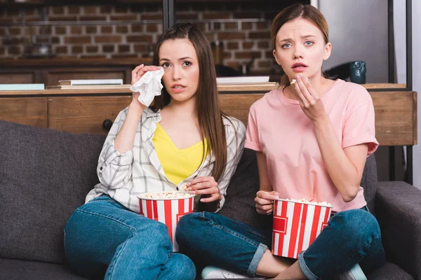 Zwei aufgebrachte Freundinnen mit Eimern Popcorn beim Filmgucken auf dem heimischen Sofa — Stockfoto