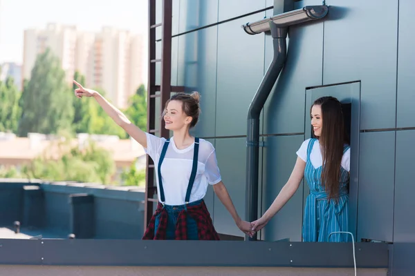 Mujer joven sonriente señalando con el dedo a una amiga sonriente en la azotea - foto de stock