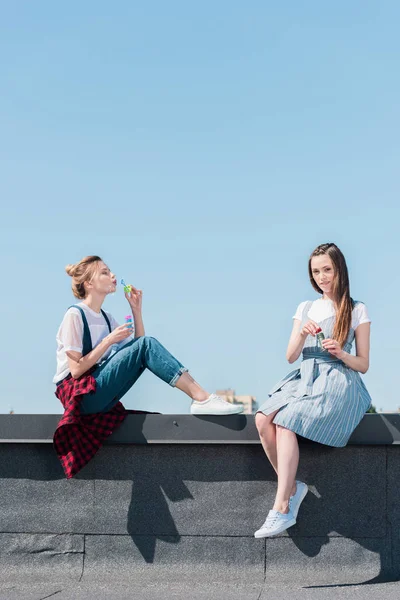 Atractivas amigas jóvenes usando sopladores de burbujas en la azotea - foto de stock