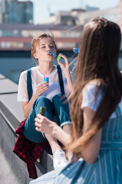 Dos amigas jóvenes con sopladores de burbujas en la azotea - foto de stock