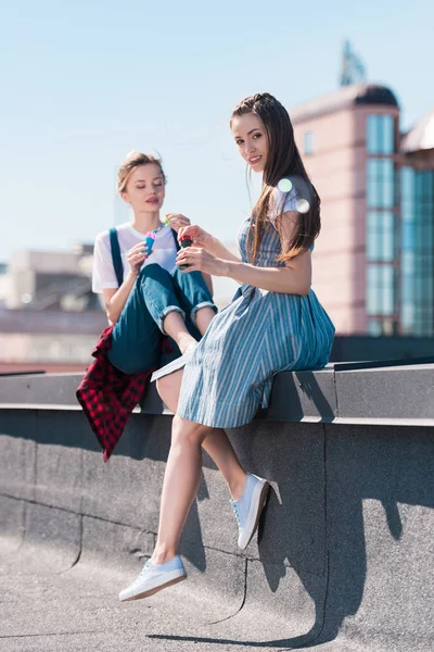 Dos amigas jóvenes usando sopladores de burbujas en la azotea - foto de stock