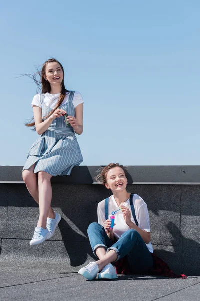 Dos amigas sonrientes usando sopladores de burbujas en la azotea - foto de stock