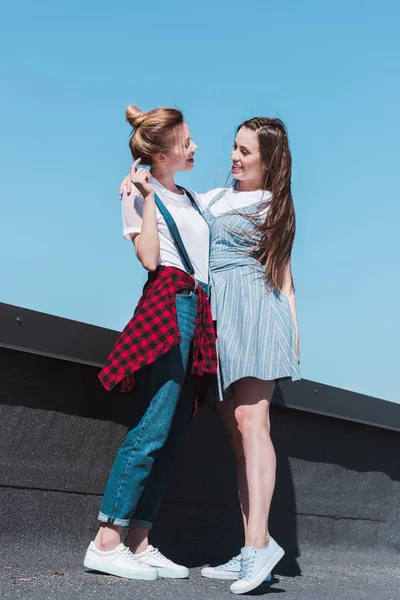 Visão de baixo ângulo de dois amigos femininos elegantes em pé no telhado — Fotografia de Stock