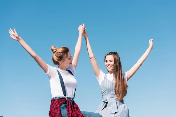 Smiling young female friends holding hands against bright blue sky — Stock Photo