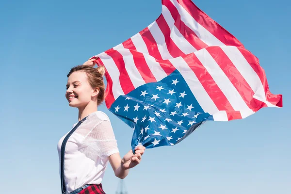 Feliz joven sosteniendo bandera de los estados unidos contra el cielo azul, concepto del día de la independencia - foto de stock