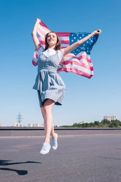 Jovem mulher pulando com bandeira dos Estados Unidos no telhado, conceito de dia de independência — Fotografia de Stock