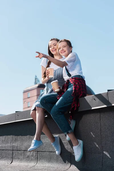 Jovem apontando por dedo para sorrir amigo feminino com xícara de papel de café no telhado — Fotografia de Stock
