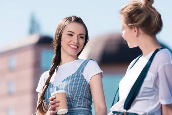 Souriant jeune femme avec tasse en papier de café parler à un ami féminin — Photo de stock
