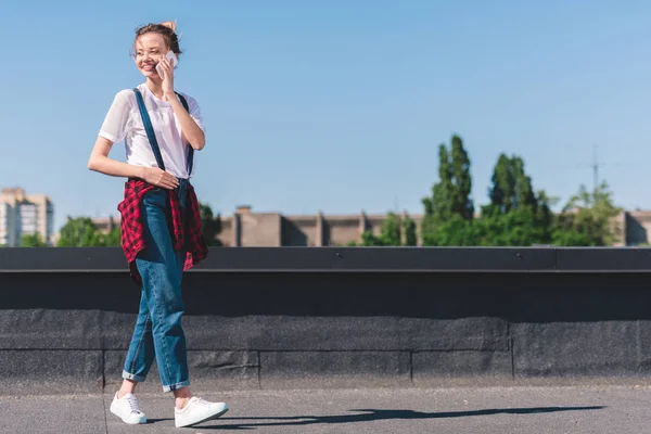Счастливая молодая женщина разговаривает по смартфону на крыше под голубым небом — стоковое фото