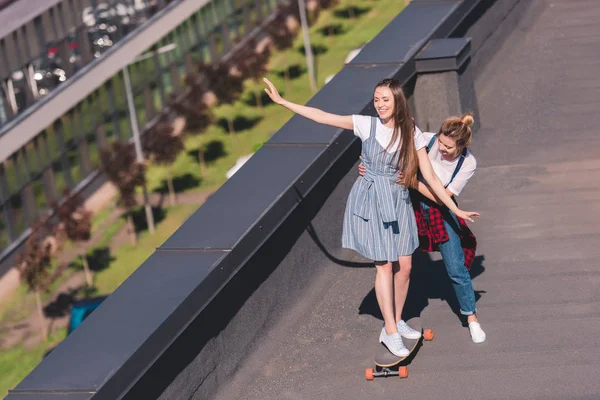 Visão de alto ângulo da mulher ensinando sua amiga montando no skate no telhado — Fotografia de Stock