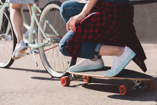 Cropped shot of woman riding bicycle and towing her female friend on skateboard — Stock Photo