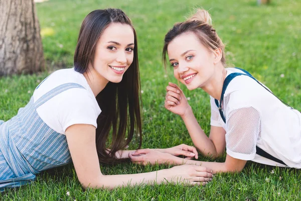 Jeunes amies souriantes allongées sur la pelouse verte dans le parc — Photo de stock