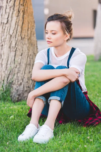 Sad young woman sitting on green lawn in park — Stock Photo