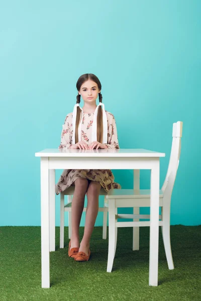 Schöne Teenie-Mädchen mit Zöpfen am Tisch sitzend, auf blau — Stockfoto