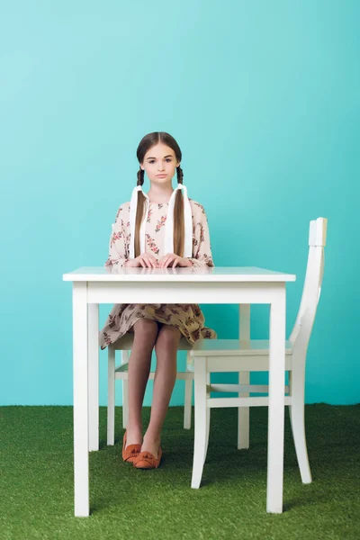 Beautiful teen girl with braids sitting at table, on blue — Stock Photo