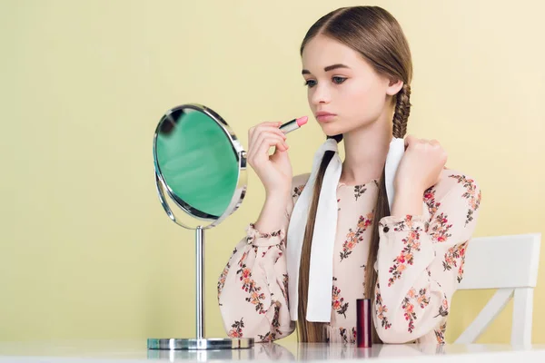 Elegant teen girl applying lipstick with mirror, isolated on yellow — Stock Photo