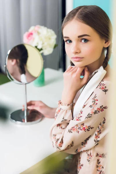 Schönes Teenie-Mädchen mit Zöpfen sitzt am Tisch mit Spiegel — Stockfoto