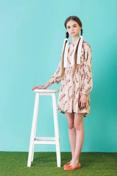 Chica adolescente de moda en vestido de verano con trenzas de pie cerca del taburete, en azul - foto de stock