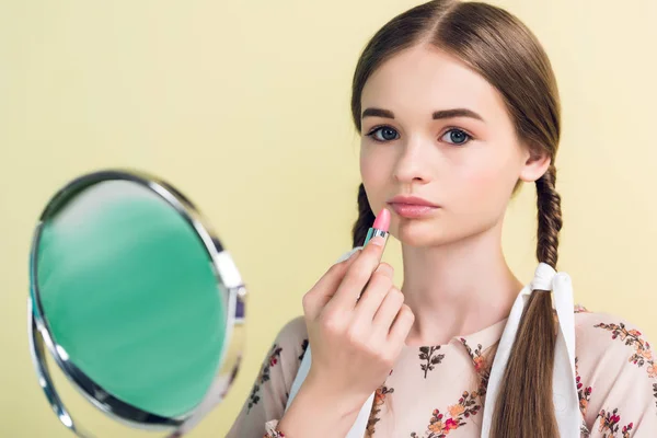 Beautiful teen girl applying lipstick with mirror, isolated on yellow — Stock Photo