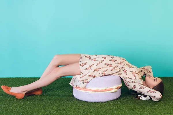 Stylish teen girl lying on big macaron — Stock Photo