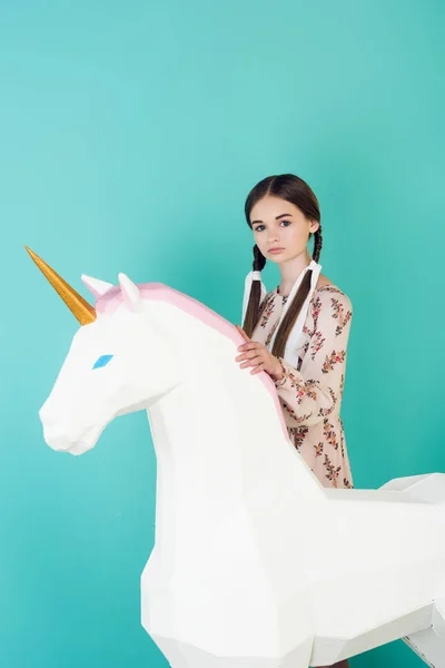 Beautiful teen girl posing with big white unicorn isolated on turquoise — Stock Photo