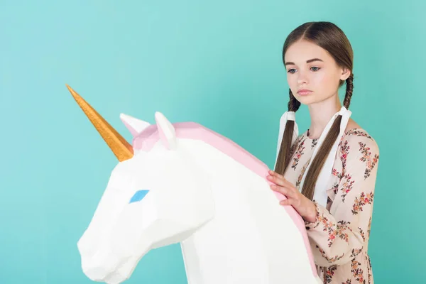 Стильна дівчина-підліток позує з великою іграшкою єдиноріг, ізольована на бірюзовому — стокове фото