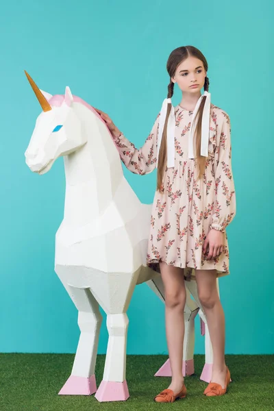 Fashionable youth girl posing with big white unicorn on turquoise — Stock Photo