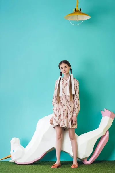 Fashionable teen girl posing with big toy unicorn upside down, on turquoise — Stock Photo