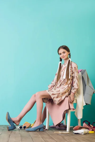 Elegante adolescente sentado en la silla con desorden de zapatos y ropa - foto de stock