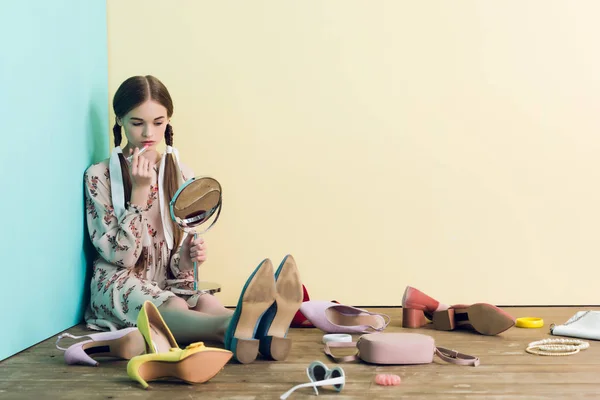 Adolescent fille appliquant maquillage avec miroir et assis sur le sol avec désordre — Photo de stock