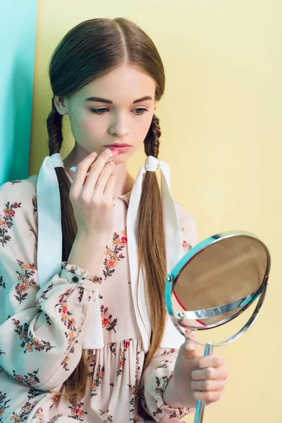 Hermosa chica adolescente con trenzas aplicación de lápiz labial con espejo - foto de stock