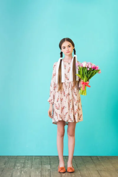 Modische schöne Mädchen mit Zöpfen im Sommerkleid hält Tulpen, auf türkis — Stockfoto