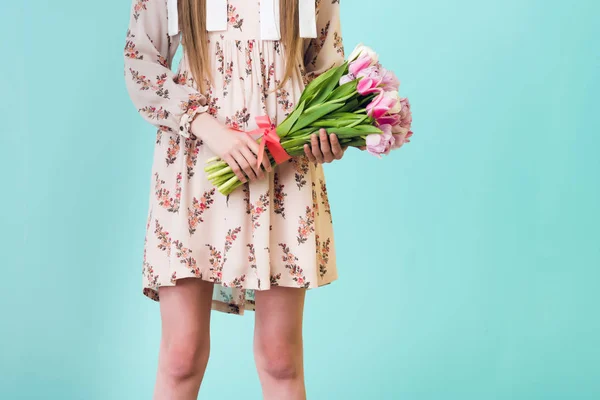 Cropped view of girl in summer dress holding bouquet of flowers, isolated on blue — Stock Photo