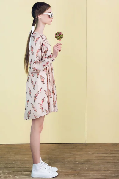 Elegante adolescente en gafas de sol con trenzas celebración de piruleta, en amarillo - foto de stock