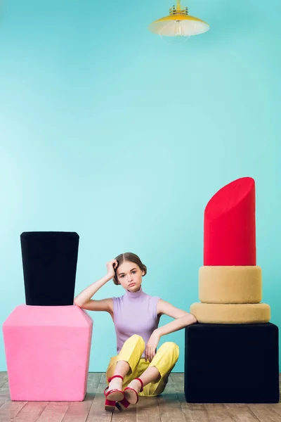 Elegant fashionable girl sitting between big nail polish and lipstick on floor — Stock Photo