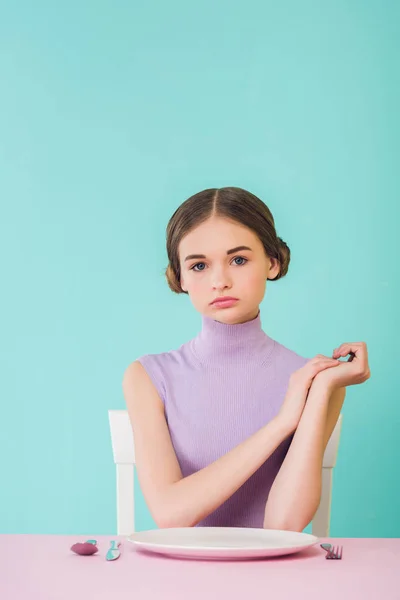 Bela menina da moda sentada à mesa com prato vazio — Fotografia de Stock