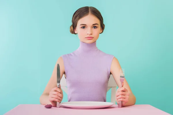 Bela menina adolescente com faca, garfo e prato vazio sentado à mesa — Fotografia de Stock