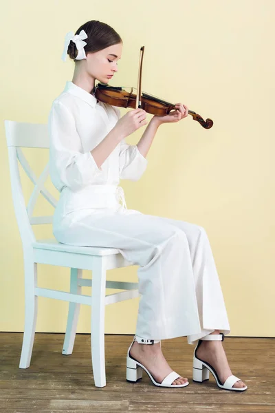Teenager im weißen Outfit spielt Geige und sitzt auf Stuhl — Stockfoto