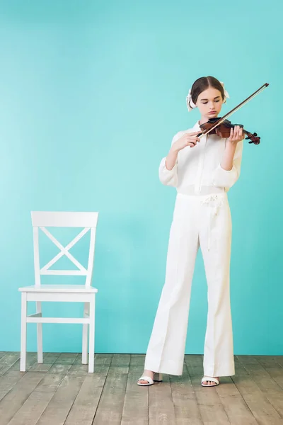 Beautiful teen girl playing violin, on blue — Stock Photo