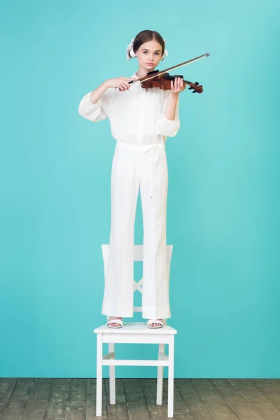 Teenie-Mädchen spielt Geige und steht auf Stuhl, auf blauem — Stockfoto
