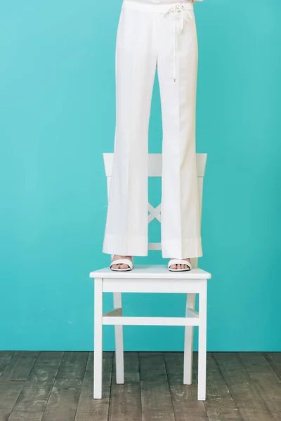 Vue de la section basse de la fille en tenue blanche élégante debout sur la chaise sur bleu — Photo de stock