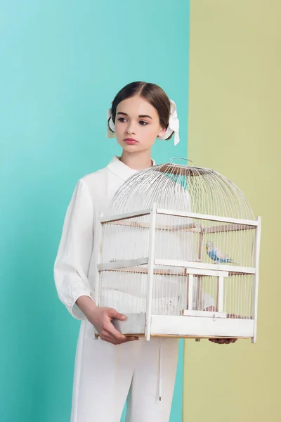 Jolie fille en tenue blanche tendance avec perroquet en cage, sur turquoise et jaune — Photo de stock