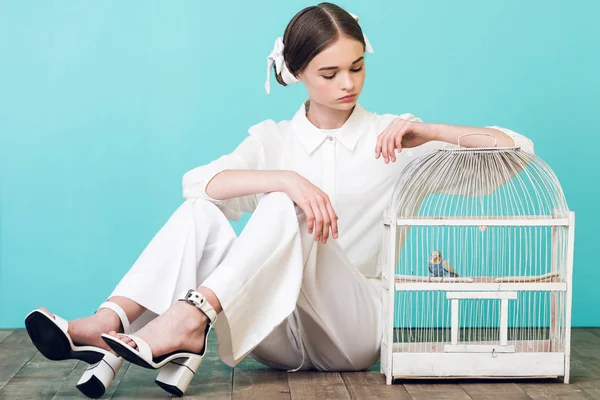 Adolescente atraente em roupa branca com papagaio na gaiola, em turquesa — Fotografia de Stock