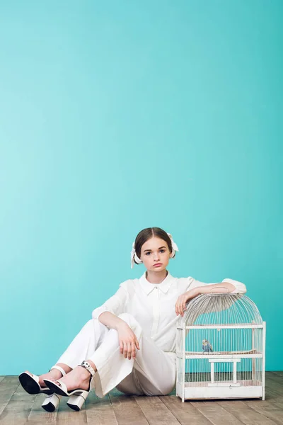 Fashionable teenager in white with parrot in cage, on turquoise — Stock Photo