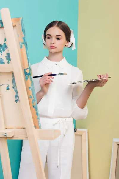 Beautiful teen artist painting on easel with brush and palette — Stock Photo