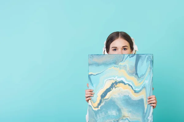 Fashionable youth girl holding blue oil painting, isolated on turquoise — Stock Photo