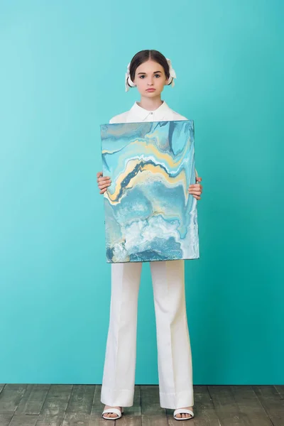 Fashionable teenager holding abstract oil painting, on turquoise — Stock Photo